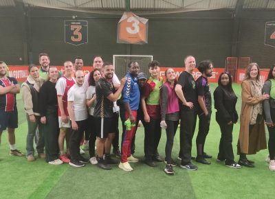 Des collègues disputent un match de foot en entreprise sur un terrain en salle, portant des dossards aux couleurs vives. Un moment de convivialité et d’esprit d’équipe illustrant la cohésion entre collaborateurs.