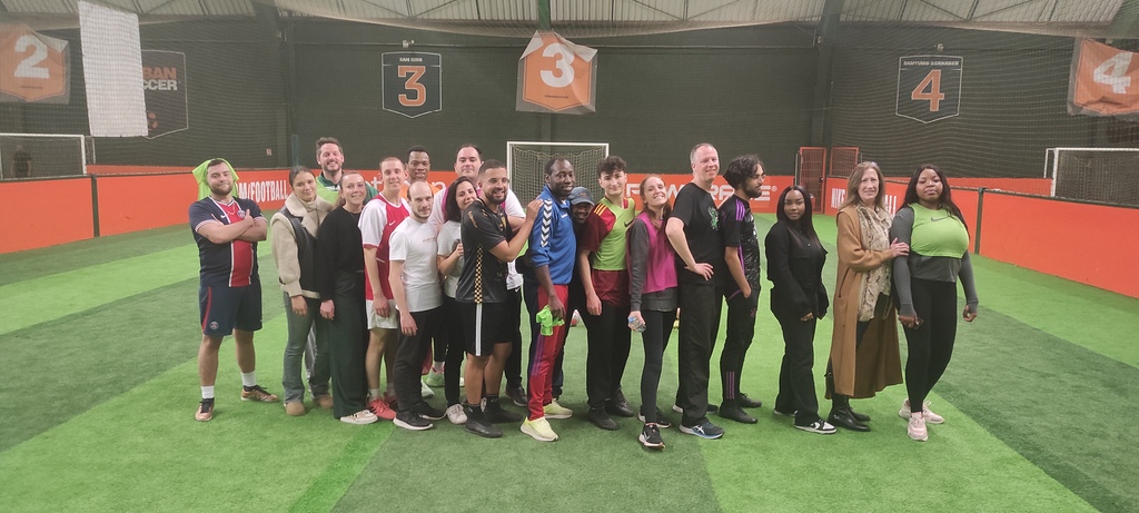 Des collègues disputent un match de foot en entreprise sur un terrain en salle, portant des dossards aux couleurs vives. Un moment de convivialité et d’esprit d’équipe illustrant la cohésion entre collaborateurs.